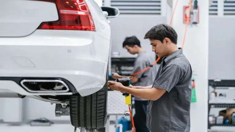 A mechanic using a pneumatic tool on a white sedan on a car lift in a european car workshop.