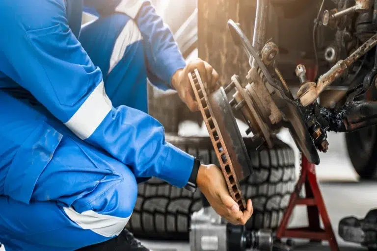 A mechanic in blue coveralls inspecting a worn brake disc, a component frequently in demand at a reliable spare parts store.