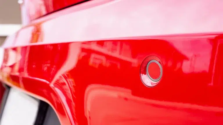 Close-up of a circular parking sensor on a bright red Mercedes bumper.