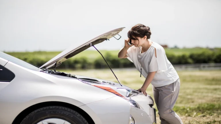 Distressed woman on her phone with a white Toyota car and its hood open, representing potential trouble from a vellfire gearbox.