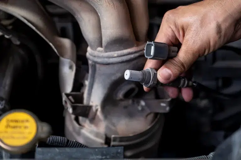 Mechanic holding an oxygen sensor, illustrating essential range rover parts on an engine.
