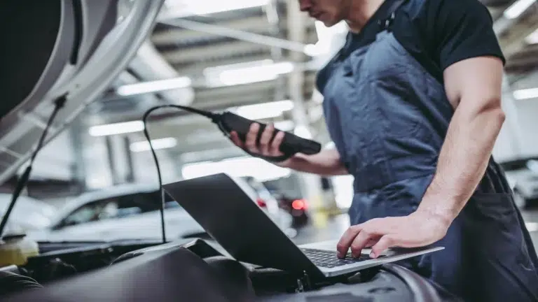 A mechanic using a diagnostic laptop and scanner tool on a vehicle with an open hood during a professional porsche car service