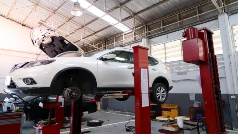 A white car raised on a hydraulic lift inside a repair shop with its hood open for maintenance, highlighting the use of genuine toyota parts malaysia.