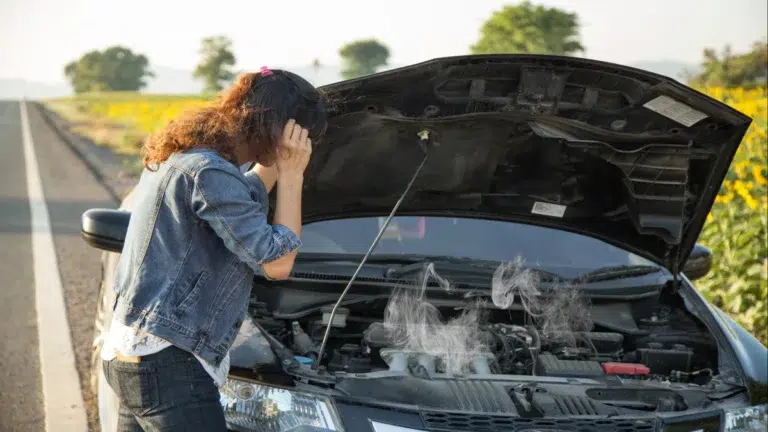 A distressed driver standing beside an overheated car with a smoking engine bay needing Toyota engine parts.